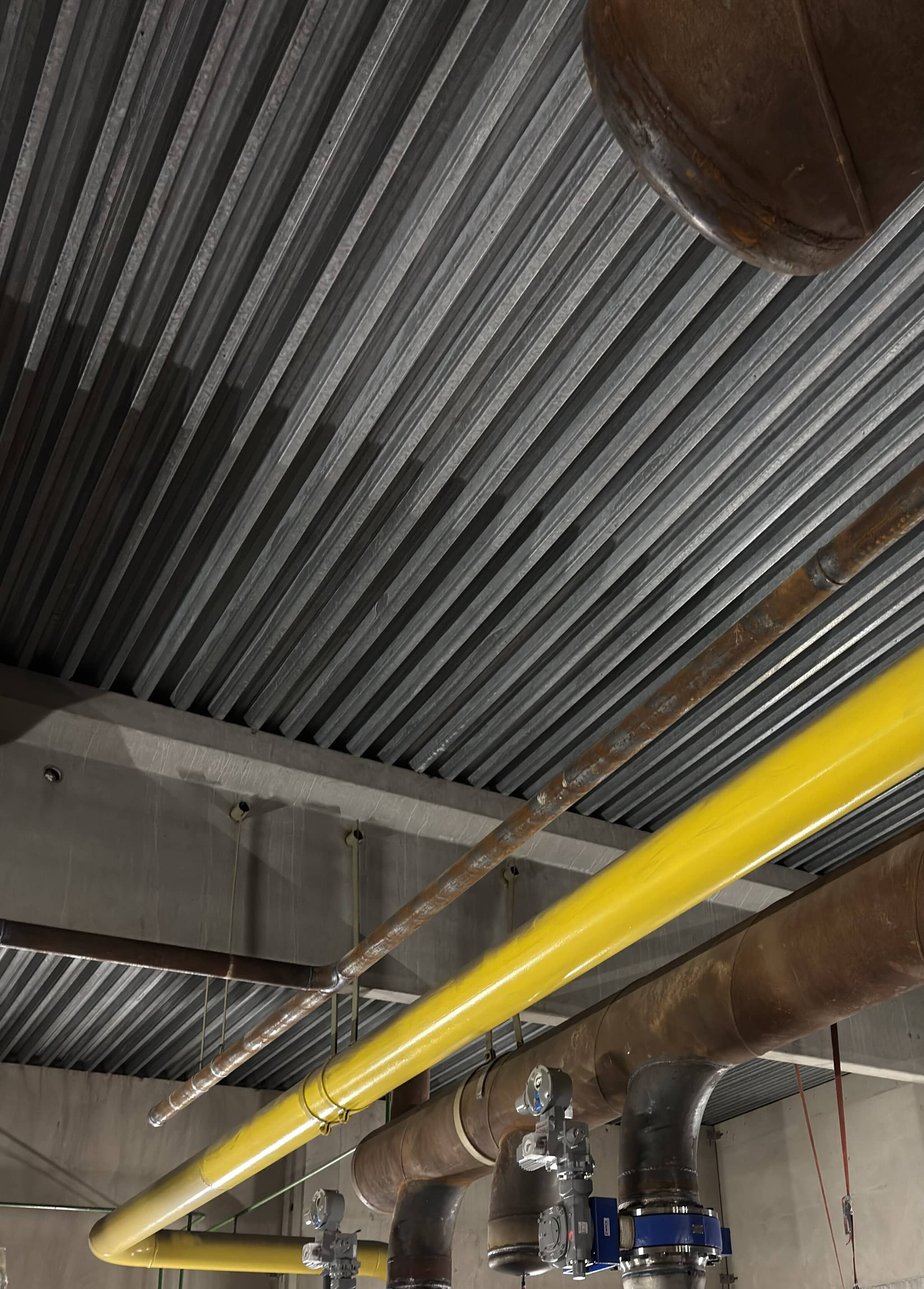 Freigelegte Rohrleitungen und Armaturen unter einer Trapezblechdecke nach dem Rückbau der Rohrdämmung