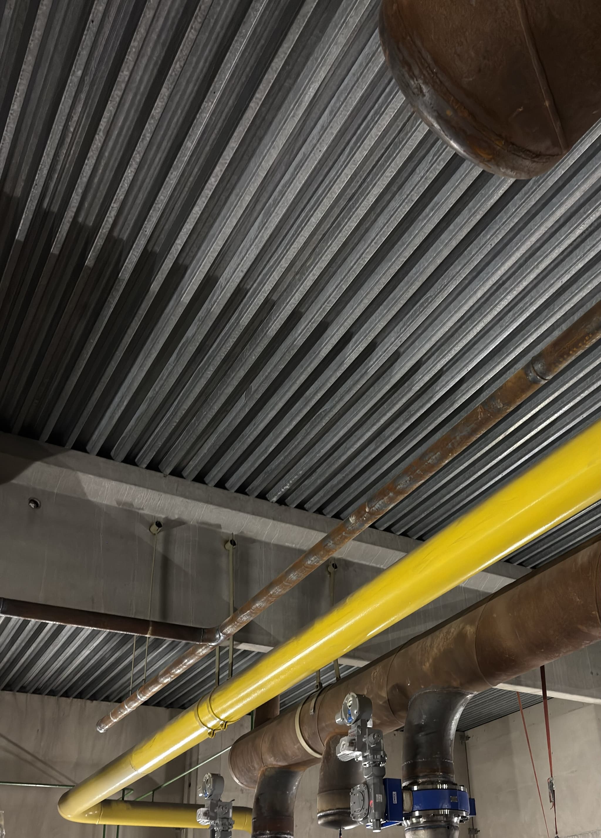 Freigelegte Rohrleitungen und Armaturen unter einer Trapezblechdecke nach dem Rückbau der Rohrdämmung
